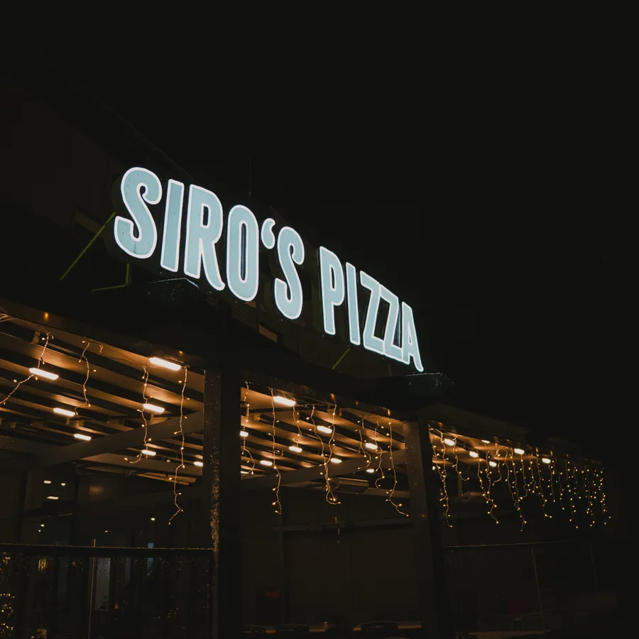 Beleuchteter Siro’s-Pizza-Schriftzug über der Terrasse am Abend