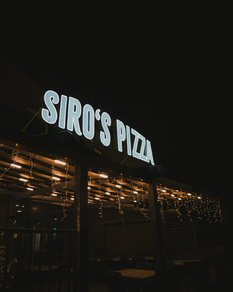 Beleuchteter Siro’s-Pizza-Schriftzug über der Terrasse am Abend
