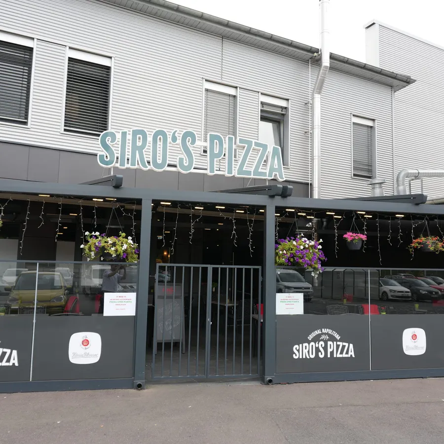 Außenansicht von Siro’s Pizza mit blumengeschmückter Terrasse